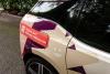 Left back side view of a BMW i3 in front of a green hedge wrapped in graphics for Pinecone Childcare in Portland, Oregon. It is mostly beige with dark purple and pink shapes. It has a red shape with a qr code and text that reads "Register now!" and "pinecone-childcare.com".