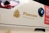 Back view of a BMW i3 wrapped in graphics for Pinecone Childcare in Portland, Oregon. It is mostly beige and has the pinecone logo on it with the slogan "Childcare done nicely" andpart of a red shape with a qr code and text that reads "Register now!" and "pinecone-childcare.com".