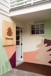 Entrance area with a wooden logo sign and a colorful mural at Pinecone Childcare in Portland, Oregon.