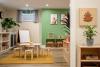 Interior view of a playroom at Pinecone childcare with a kids' table, an easle, shelves and a wooden sign with a pinecone logo on it.